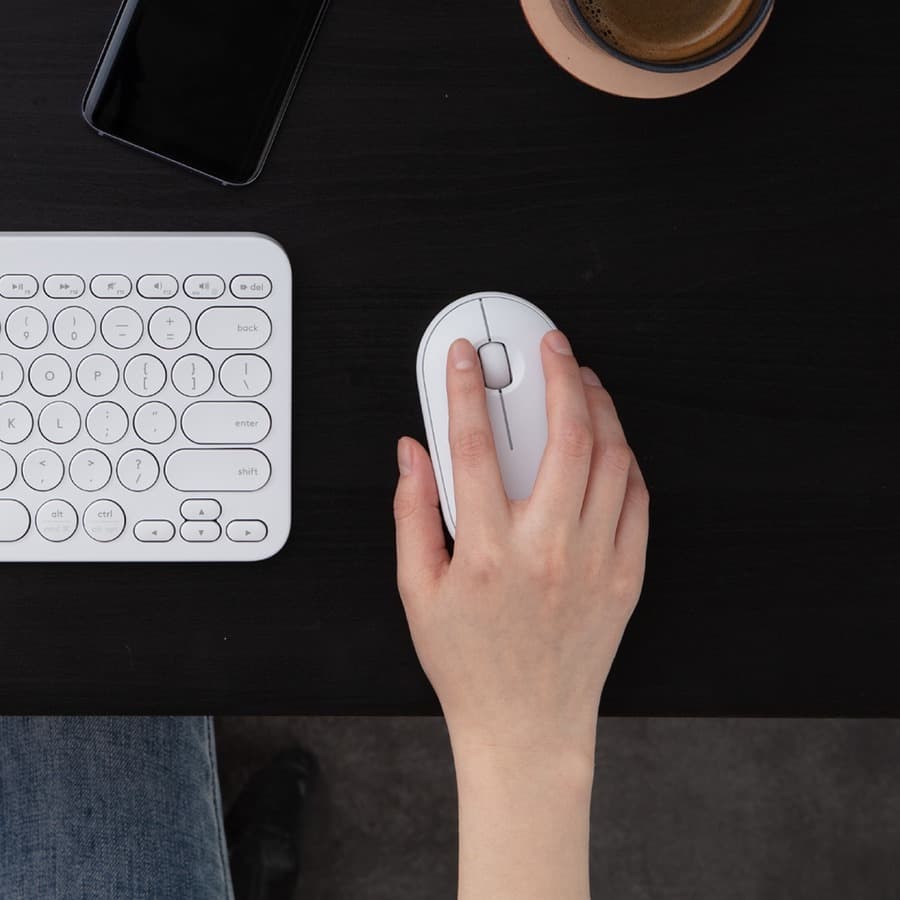 Logitech Pebble M350 wireless mouse in off white shown on a desk beside a laptop